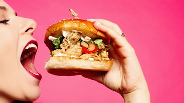 Eine Frau beißt in einen Burger, der mit Fleisch belegt ist. Bei einer Fleischallergie, auch Alpha-Gal-Syndrom genannt, kann es zu allergischen Symptomen kommen. | Bild: colourbox.com