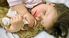 Das dreijährige Mädchen Amy schläft mit ihrem Teddy im Arm. | Bild: picture-alliance/dpa