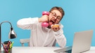 Zu viel Multitasking ist nicht gesund. Es verursacht Stress und kann auf Dauer zu einem Burnout oder zu einer Depression führen. Im Bild: Ein Mann sitzt am Schreibtisch vor dem Computer, hält in einer Hand eine Hantel in der andern ein Stück Kuchen. | Bild: picture alliance / Zoonar | Khosrow Rajab Kordi