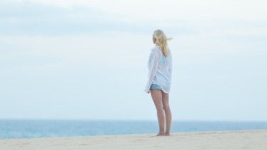 Eine Frau steht am Strand und blickt hinaus aufs Meer.  | Bild: colourbox.com
