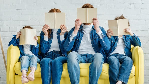 Eine vierköpfige Familie sitzt auf einer Coach und steckt die Köpfe in Bücher. Bildung kann uns bis ins hohe Alter fit halten. | Bild: colourbox.com