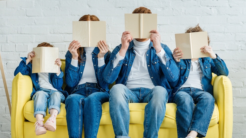 Eine vierköpfige Familie sitzt auf einer Coach und steckt die Köpfe in Bücher. Bildung kann uns bis ins hohe Alter fit halten. | Bild: colourbox.com