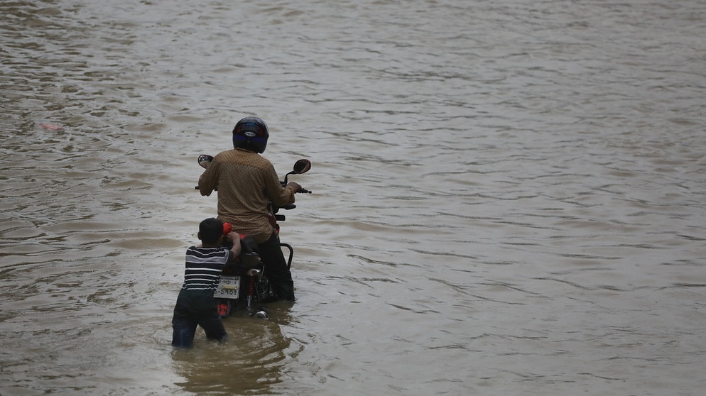 Ein Kind schiebt ein Motorrad in einem überfluteten Gebiet. Biodiversität und Klimawandel hängen eng miteinander zusammen.  | Bild: picture-alliance/dpa