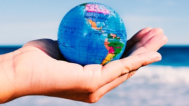 Eine Hand hält einen Globus. Im Hintergrund ist das Meer zu sehen. Auf der UN-Biodiversitätskonferenz 2022 sollen gemeinsame Lösungen gefunden werden. | Bild: colourbox.com