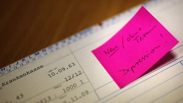 Auf der Karteikarte eines Patienten einer Arztpraxis klebt ein Zettel «Neu/Ohne Termin Depression!».  | Bild: dpa-Bildfunk/Arno Burgi