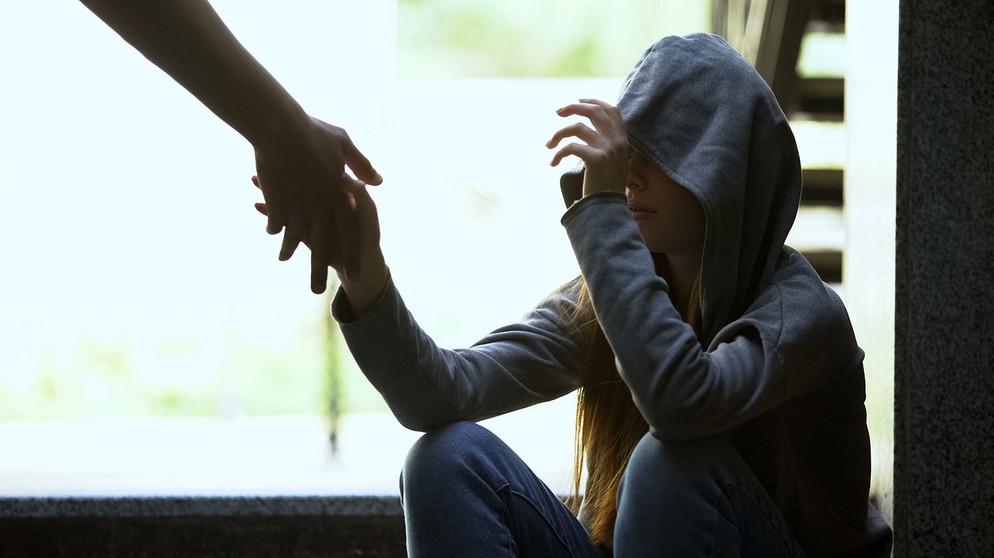 Einer sitzenden Jugendlichen wird eine Hand gereicht. Für Jugendliche ist Cannabis besonders gefährlich. Sie entwickeln nach Cannabis-Konsum häufiger Psychosen und andere Erkrankungen.  | Bild: colourbox.com