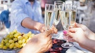 Mehrere Menschen stoßen an einem gedeckten Tisch mit Champagner an. | Bild: picture-alliance/dpa