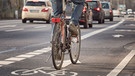 Ein Fahrradfahrer fährt im Straßenverkehr auf einer Fahrradspur neben Autos. Wer mit dem Fahrrad statt dem Auto unterwegs ist, spart CO2-Emissionen ein. Das könnte sich bei einem Pro-Kopf-CO2-Budget auswirken. | Bild: stock.adobe.com/Kara