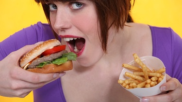 Warum essen wir ungesund? Dieser Frage geht die Sendung "alles wissen" nach. Im Bild: Frau mit Pommes-Frites-Tüte in der Hand beißt in einen Hamburger | Bild: colourbox.com