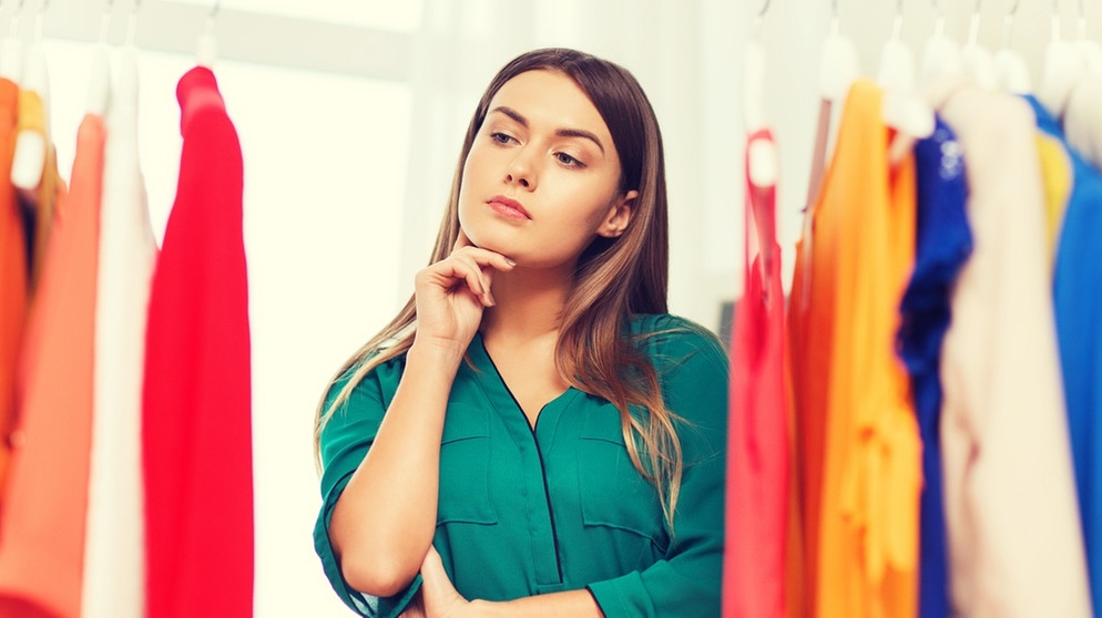 Eine Frau steht vor einer Kleiderstange und überlegt, welche Kleidung sie anziehen soll. Shopping kann auch  umweltfreundlich sein.  | Bild: colourbox.com