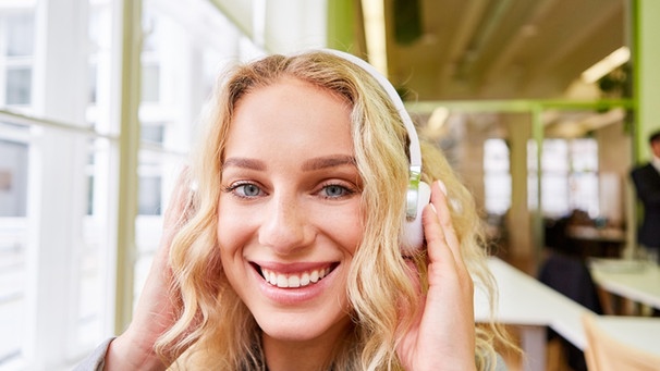 Eine lächelnde blonde Frau mit Kopfhörern schaut in die Kamera. | Bild: picture-alliance/dpa Zoonar | Robert Kneschke