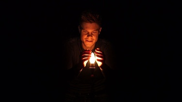 Moderator mit Lampe, um ihn herum Dunkelheit | Bild: BR