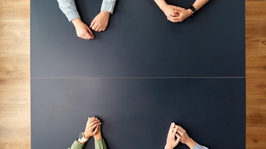 An einem Tisch sieht man die Hände von vier Menschen, die sich gegenübersitzen. | Bild: picture alliance / Zoonar | lev dolgachov