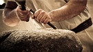 Ein Bildhauer bearbeitet einen massiven Stein mit Hammer und Meißel. | Bild: stock.adobe.com/Piga