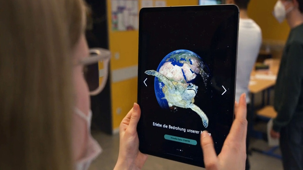 Eine Schülerin nutzt die WDR-Klima-App auf einem Tablet, das eine Weltkugel und eine Schildkröte zeigt. | Bild: WDR