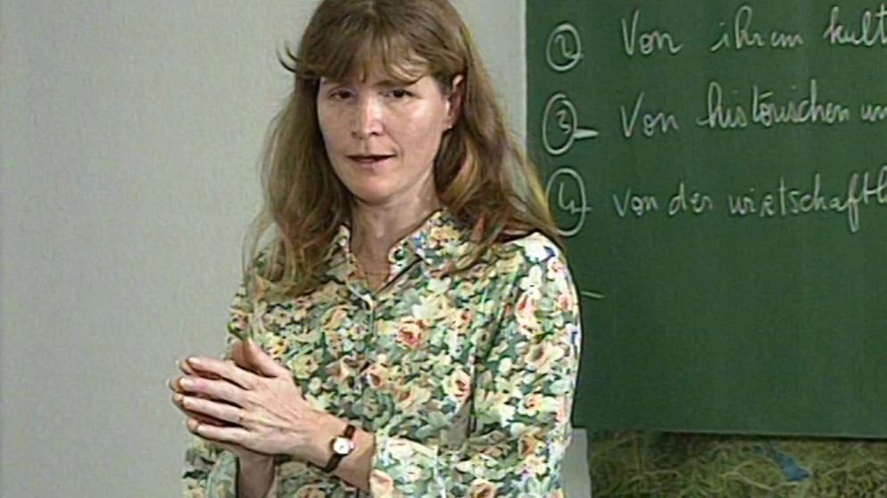 Deutschlehrerin Christine steht im Klassenzimmer vor der Tafel. | Bild: BR