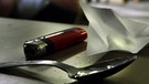 Drogenutensilien auf dem Tisch und verschwommen ein Mann im Hintergrund | Bild: Getty Images