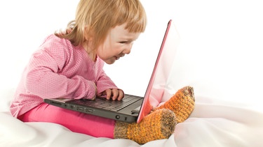 rosarot gekleidetes kleines Mädchen sitzt vor einem Laptop auf dem Bett | Bild: colourbox.com