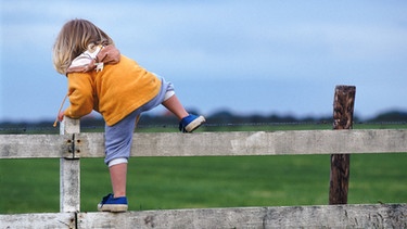 Ein Mädchen klettert über einen Zaun | Bild: John Foxx Images