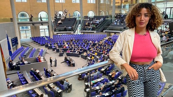Reporterin Tessniem steht vor einer Glasabtrennung und schaut in die Kamera. Unter ihr ist der Plenarsaal mit Abgeordneten des Deutschen Bundestages. | Bild: WDR | tvision