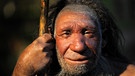 Ein nachgebauter Neandertaler mit einem Holzstab in der Hand lächelt. Das Neandertaler-Genom gibt auch Rückschlüsse auf homo sapiens.  | Bild: picture-alliance/dpa