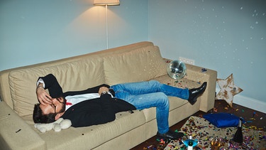 Wenn nach zu viel Alkohol Erinnerungslücken entstehen, spricht man auch von einem "Filmriss". Im Bild: Mann nach einer feucht-fröhlichen Feier auf der Couch. | Bild: picture-alliance/dpa