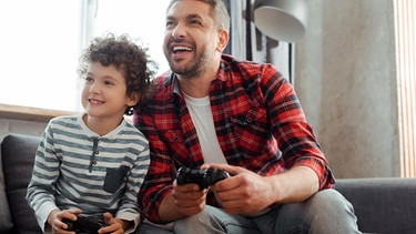 Vater und Kind spielen Computerspiele und halten eine Spielkonsole in der Hand. | Bild: colourbox.com