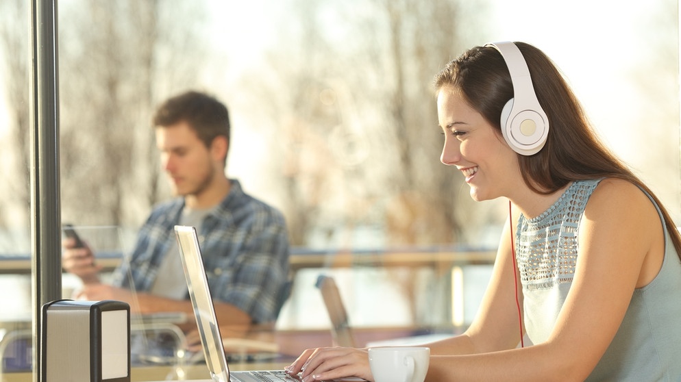 Eine Frau mit Kopfhörern sitzt vor einem Laptop. Im Hintergrund sitzt ein Mann. Wir erklären euch, mit welchen Strategien und Techniken ihr, besser lernt, eure Motivation erhöht und eure Lernziele erreicht. | Bild: colourbox.com