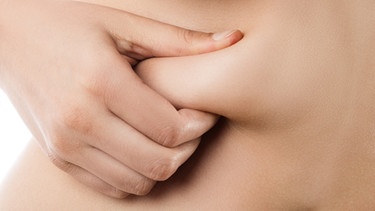 Eine Frau untersucht ein Fettröllchen an ihrem Bauch. | Bild: picture-alliance/Zoonar|A.Tugolukov