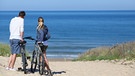 Ein Mann und eine Frau stehen mit ihren Fahrrädern am Strand. Nachhaltiges Reisen kann funktionieren.  | Bild: colourbox.com