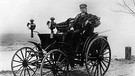 Carl Friedrich Benz (r.) steuert im Jahr 1894 einen seiner Wagen. Der Ingenieur und Automobilkonstrukteur Carl Friedrich Benz gründete 1883 die Firma Benz & Cie., Rheinische Gasmotorenfabrik, die sich 1926 mit der Daimler-Motoren-Gesellschaft zur Daimler-Benz AG zusammentat. | Bild: picture-alliance/dpa