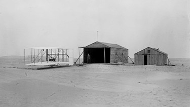 Wartungshalle der Wrights bei Kitty Hawk. Orville und Wilbur Wright machten einen Menschheitstraum wahr: Sie bauten ein Fluggerät mit Lenkung und eigenem Antrieb. Damit kamen die beiden Brüder dem Traum vom Fliegen ein gewaltiges Stück näher. | Bild: picture-alliance/dpa