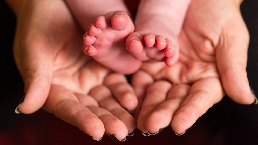 Babyfüßchen werden in Händen gehalten. Viele Menschen können sich ihren Kinderwunsch nicht auf natürliche Weise erfüllen. Für immer mehr von ihnen wird Reproduktionsmedizin zur Alternative. Wie funktioniert künstliche Befruchtung? | Bild: picture-alliance/empics | Dominic Lipinski