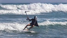 Ein als Sensemann verkleideter Surfer reitet auf einer Welle.  | Bild: picture-alliance/dpa