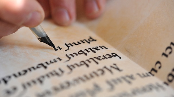 Ein Mann schriebt nach mittelalterlichem Vorbild Buchstaben in ein Buch aus Pergament.  | Bild: picture-alliance/ dpa | Bernd Thissen