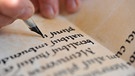 Ein Mann schriebt nach mittelalterlichem Vorbild Buchstaben in ein Buch aus Pergament.  | Bild: picture-alliance/ dpa | Bernd Thissen