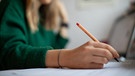 Eine junge Lehrerin korrigiert mit der Hand die Hausaufgaben. | Bild: BR/Johanna Schlüter