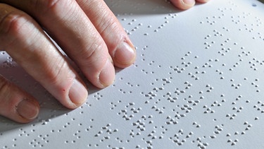 Zwei Hände ertasten die Punkte der Brailleschrift oder auch Blindenschrift. Dank der Brailleschrift können Blinde mit den Fingern lesen. In der Blindenschrift ist jeder Buchstabe des Alphabets mit Punkten dargestellt. Hier erfahrt ihr, wie Louis Braille, selbst blind, im Alter von 16 Jahren die Punktschrift entwickelte. | Bild: picture-alliance/dpa