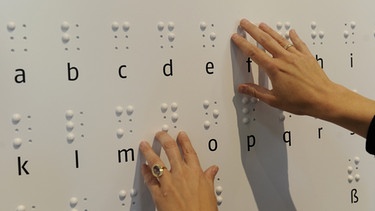 Zwei Hände ertasten das Alphabet der Brailleschrift oder auch Blindenschrift auf einer Tafel. Dank der Brailleschrift können Blinde mit den Fingern lesen. In der Blindenschrift ist jeder Buchstabe des Alphabets mit Punkten dargestellt. Hier erfahrt ihr, wie Louis Braille, selbst blind, im Alter von 16 Jahren die Punktschrift entwickelte. | Bild: picture-alliance/dpa