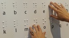 Zwei Hände ertasten das Alphabet der Brailleschrift oder auch Blindenschrift auf einer Tafel. Dank der Brailleschrift können Blinde mit den Fingern lesen. In der Blindenschrift ist jeder Buchstabe des Alphabets mit Punkten dargestellt. Hier erfahrt ihr, wie Louis Braille, selbst blind, im Alter von 16 Jahren die Punktschrift entwickelte. | Bild: picture-alliance/dpa