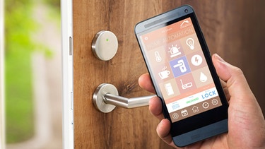 Ein Mann nutzt sein Handy mit einer Smarthome-Sicherheits-App, um die Tür seines Hauses zu entriegeln. | Bild: picture alliance / Panther Media | Alexander Kirch