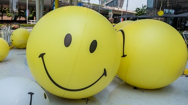 Große Bälle mit Smiley-Gesichtern liegen vor einem Kaufhaus | Bild: picture-alliance/Wang Gang/Costfoto
