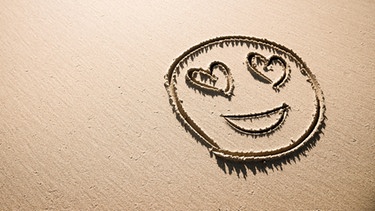 Ein in den Sand gezeichnetes Emoji mit Herzchenaugen | Bild: colourbox.com