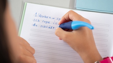 Eine Schülerin einer Grundschule schreibt Verben in ihr Heft.   | Bild: dpa-Bildfunk/Sebastian Gollnow