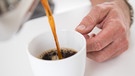 In vielen Lokalen wird zum Kaffee ein Glas Wasser serviert. Macht das Sinn? Auf diesem Bild gießt sich ein Mann eine Tasse Kaffee ein.  | Bild: picture alliance/dpa Themendienst