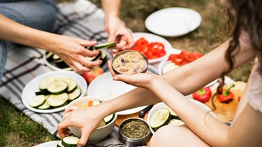 Entspannt mit Freunden essen ist allemal gesünder als alleine vor dem Fernseher. Hier bereiten zwei junge Leute ein Picknick vor.  | Bild: colourbox.com