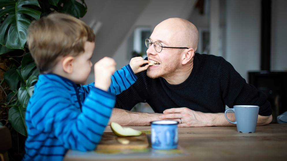 Auch bei Stress: Essen nicht vergessen! Im Bild: Ein Kind füttert seinen Vater mit Obst am Esstisch.  | Bild: picture-alliance/dpa/ photothek/Janine Schmitz