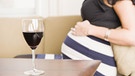 Glas Rotwein auf einem Tisch, schwangere Frau hinten | Bild: picture alliance/imageBROKER