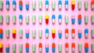 Gerade angeordnet einzelne Tabletten in unterschiedlichen Farben auf rosa Untergrund in vier Reihen. Geht es nach der Werbung, benötigen wir alle zusätzliche Vitamine und Mineralstoffe für unsere Gesundheit. Aber stimmt das? | Bild: picture alliance / Zoonar | Alexander Limbach