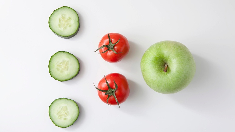 Auf einem weißen Untergrund ist ein Dreieck aus Gemüse und Obst zu sehen. Links untereinander drei Scheiben Gurke, rechts daneben zwei kleine Tomaten und wieder rechts daneben ein Apfel. Jedes Land hat seine eigene Lebensmittelpyramide, die darstellen soll, wie viel man von welchen Lebensmitteln zu sich nehmen sollte. "Nur eine Pille am Tag für ein gesundes Immunsystem" - Werbung suggeriert, dass wir Nahrungsergänzungsmittel wie Vitaminkapseln brauchen. Aber stimmt das? | Bild: picture alliance / imageBROKER | Pierre Pavot